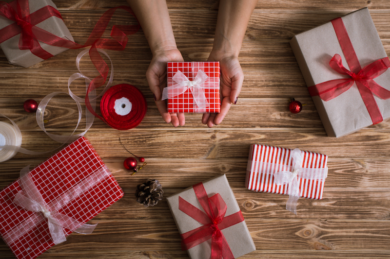 Female hands wrapping xmas gifts into paper and tying them up with red and white threads
